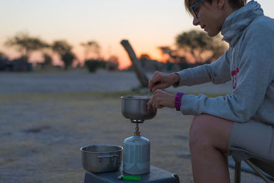 Side view of woman making tea on burner at dusk