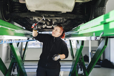 Female mechanic examining car with hammer in auto repair shop