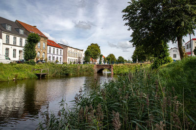 Canal amidst trees and buildings against sky