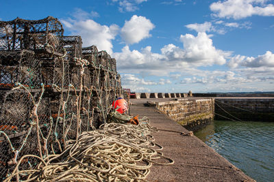 Stack of old fishing net by sea against sky