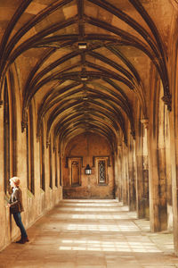 Full length of woman looking through window while standing in corridor