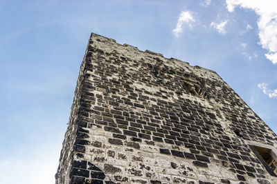 The ruins of a historical tower against a blue sky with white clouds.