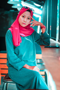 Portrait of young woman in hijab on chair by table