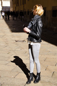 Side view of young woman standing on paved footpath in city