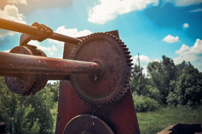 Close-up of rusty machine part on field against sky