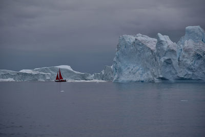 Scenic view of red sails against huge icebergs 