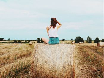 Rear view of woman sitting on field against sky