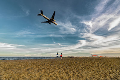 Low angle view of airplane flying over beach against sky