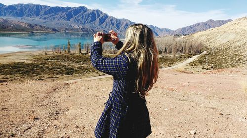 Rear view of woman photographing mountain through smart phone on sunny day