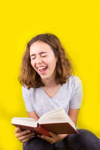 Beautiful young woman reading book against yellow background