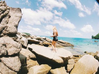 Woman standing on rock by sea against sky