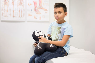 Portrait of boy holding skeleton stuffed toy on examination table at orthopedic clinic