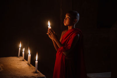 Young woman standing against illuminated candles in temple