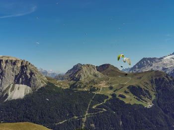 Scenic view of mountains with people paragliding against blue sky