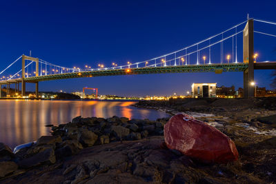Illuminated bridge over a river with a red boulder in the foreground