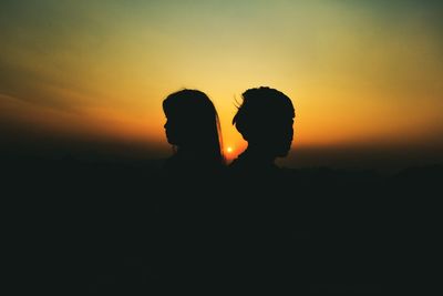 Side view of silhouette people back to back against orange sky during sunset