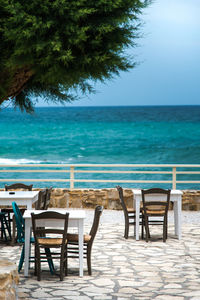 Empty chairs and table by swimming pool against sea
