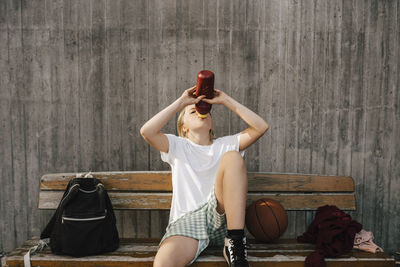 Exhausted girl drinking water while sitting on bench