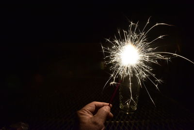 Cropped hand of man with burning sparkler at night