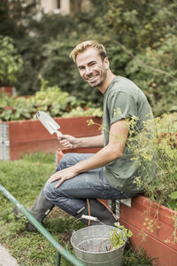 Full length portrait of happy man with gardening equipment sitting in garden