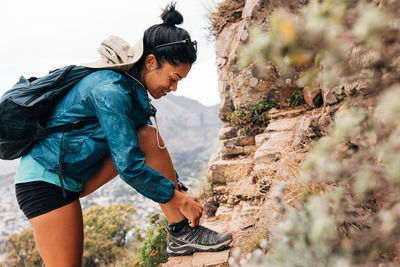 Side view of woman tying shoelace on rock