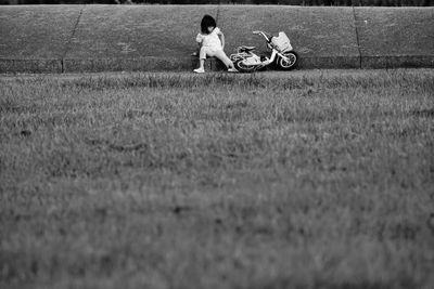 Girl with bicycle sitting on field