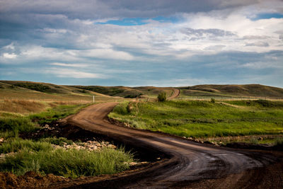 Dirt road on landscape against cloudy sky