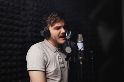 Man sings into microphone, professional recording studio, headphones. black soft walls,