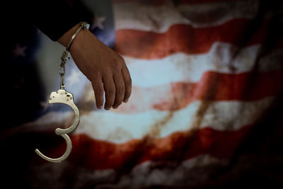 Cropped hand of male criminal with handcuffs against american flag