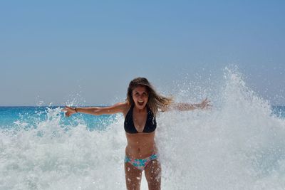 Woman with arms raised splashing water in sea against sky