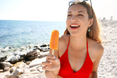 Brazilian laughing girl eating orange ice lolly on the beach on summer