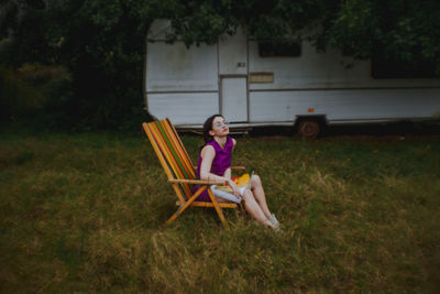 Woman with magazine sitting on chair over field