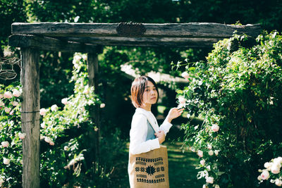 Woman standing by plants against trees