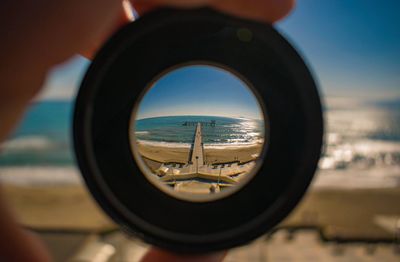 Cropped hand holding lens against pier