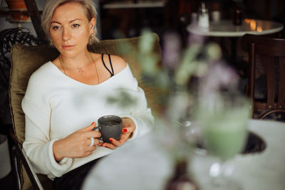 Middle age thoughtful woman holding cup of tea while sitting in cafe