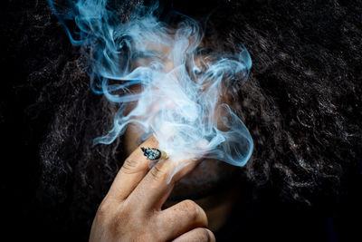 Close-up of hand holding cigarette against black background