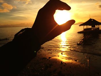Close-up of silhouette hand on beach during sunset