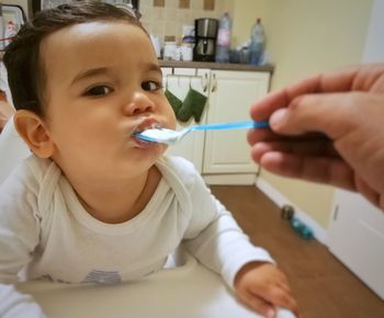 Cropped hand of parent feeding son on high chair at home