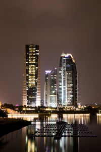 Illuminated buildings by river against sky in city at night