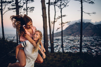 Happy woman piggybacking friend in forest