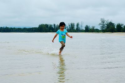 Cheerful girl running in sea against sky