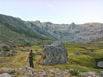 Side view of hiker standing on field against sky