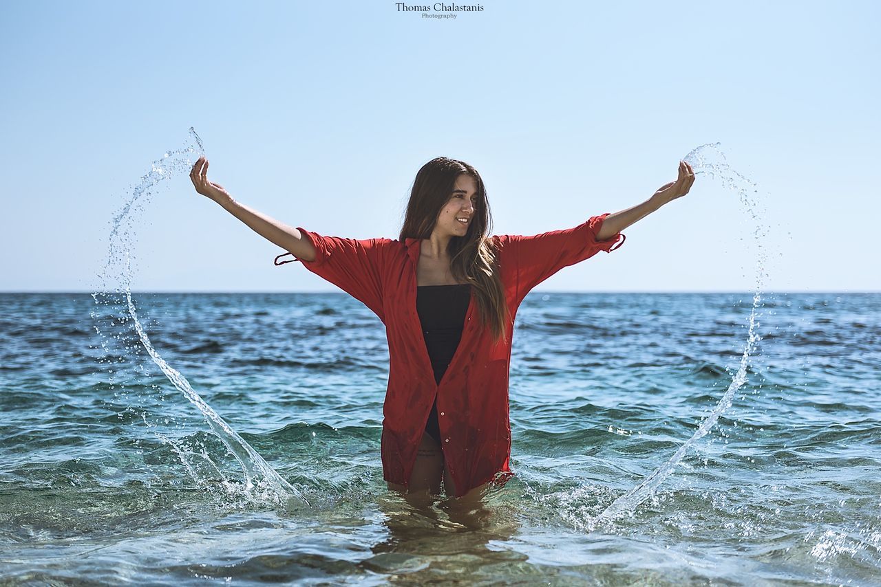 one person, young adult, standing, young women, front view, looking at camera, real people, sky, portrait, sea, red, day, full length, lifestyles, water, leisure activity, balance, outdoors, clear sky, beauty in nature, beautiful woman, smiling, happiness, nature, horizon over water, people