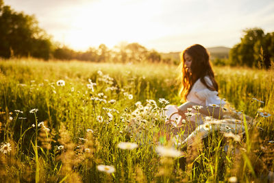 Side view of woman standing amidst flowers on field