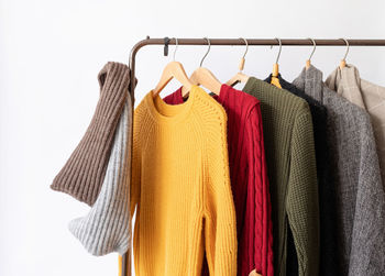 Row of different colorful knitted sweaters hang on hangers, white background