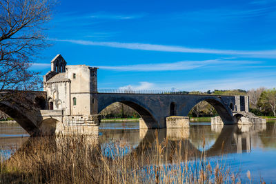 Arch bridge over river by building against blue sky