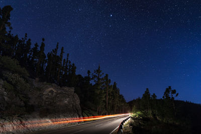 Road amidst trees against sky at night