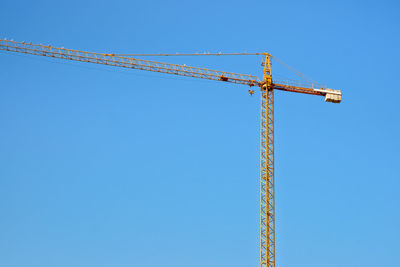 Low angle view of crane against clear blue sky