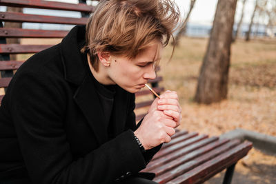 Young man lighting cigarette while sitting at park