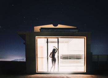Woman standing at home seen through window during night